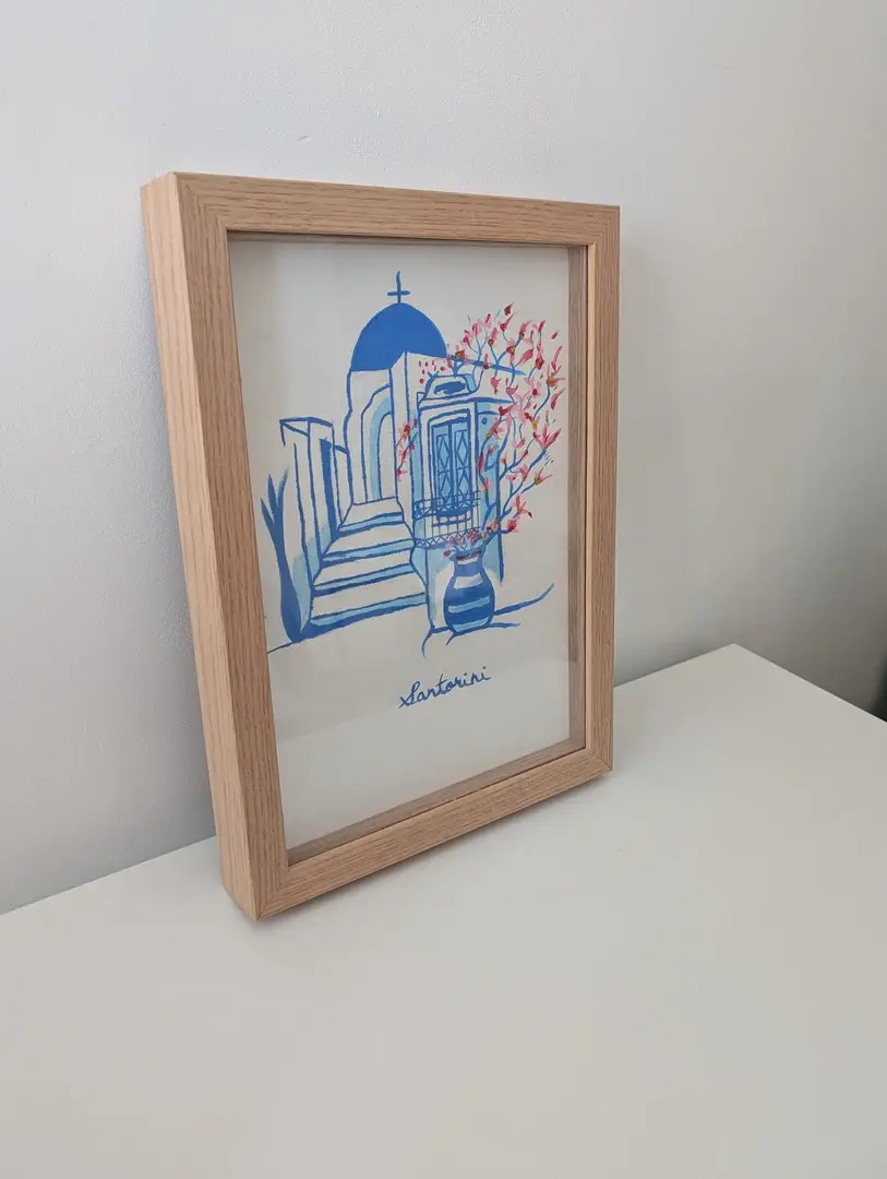 Cadre Alba profond en bois clair posé de trois-quarts sur un meuble blanc, dessin bleu de Santorin