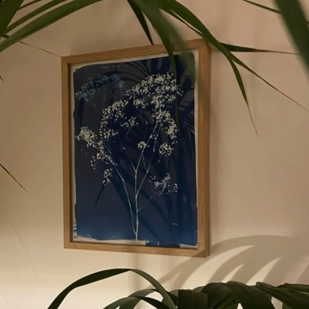 Cadre Charlotte en bois clair au mur, cyanotype bleu de fleurs derrière des palmes