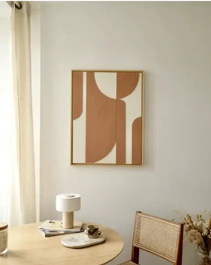 Cadre fin en bois clair au mur, œuvre abstraite terracotta et crème au-dessus d'une table ronde