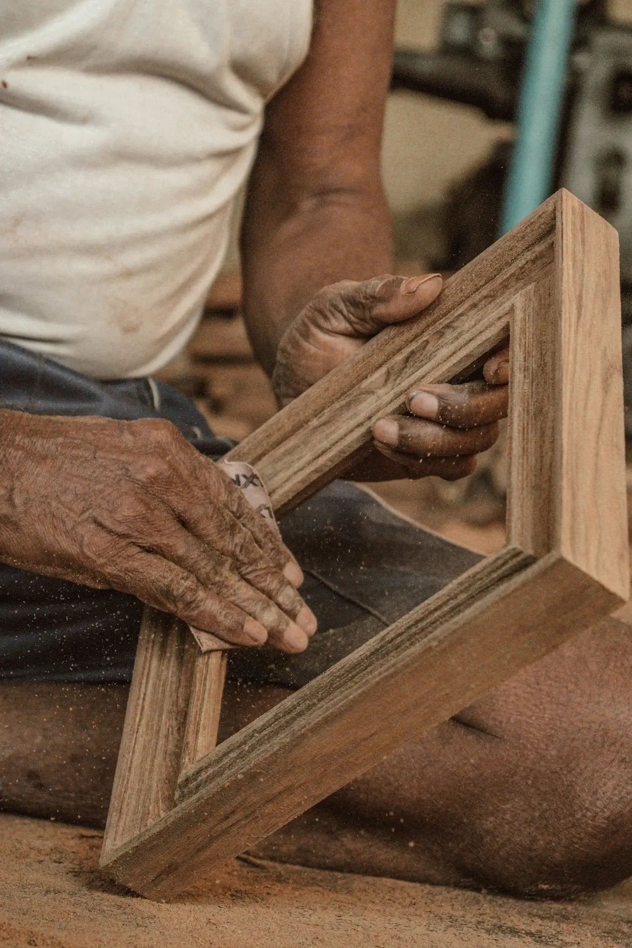 Mains d'un artisan tenant un cadre en bois non fini, avec de la sciure