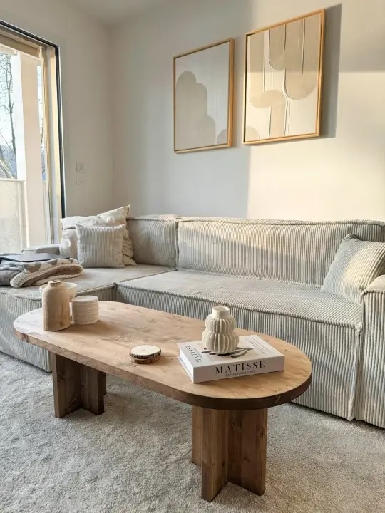 Salon avec canapé en velours côtelé beige et table basse en bois, deux cadres en bois clair à œuvres abstraites