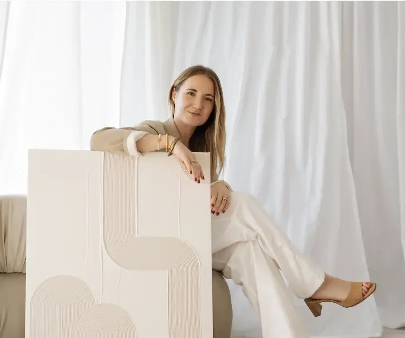 Femme assise tenant une grande toile en relief crème devant des rideaux blancs