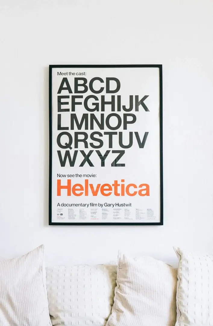 Cadre noir fin encadrant une affiche typographique, posé parmi des coussins blancs