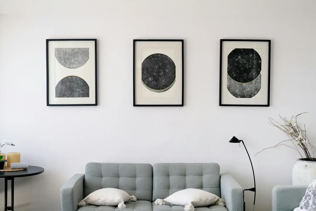 Trois cadres noirs à passe-partout, estampes circulaires noires au-dessus d'un canapé capitonné gris